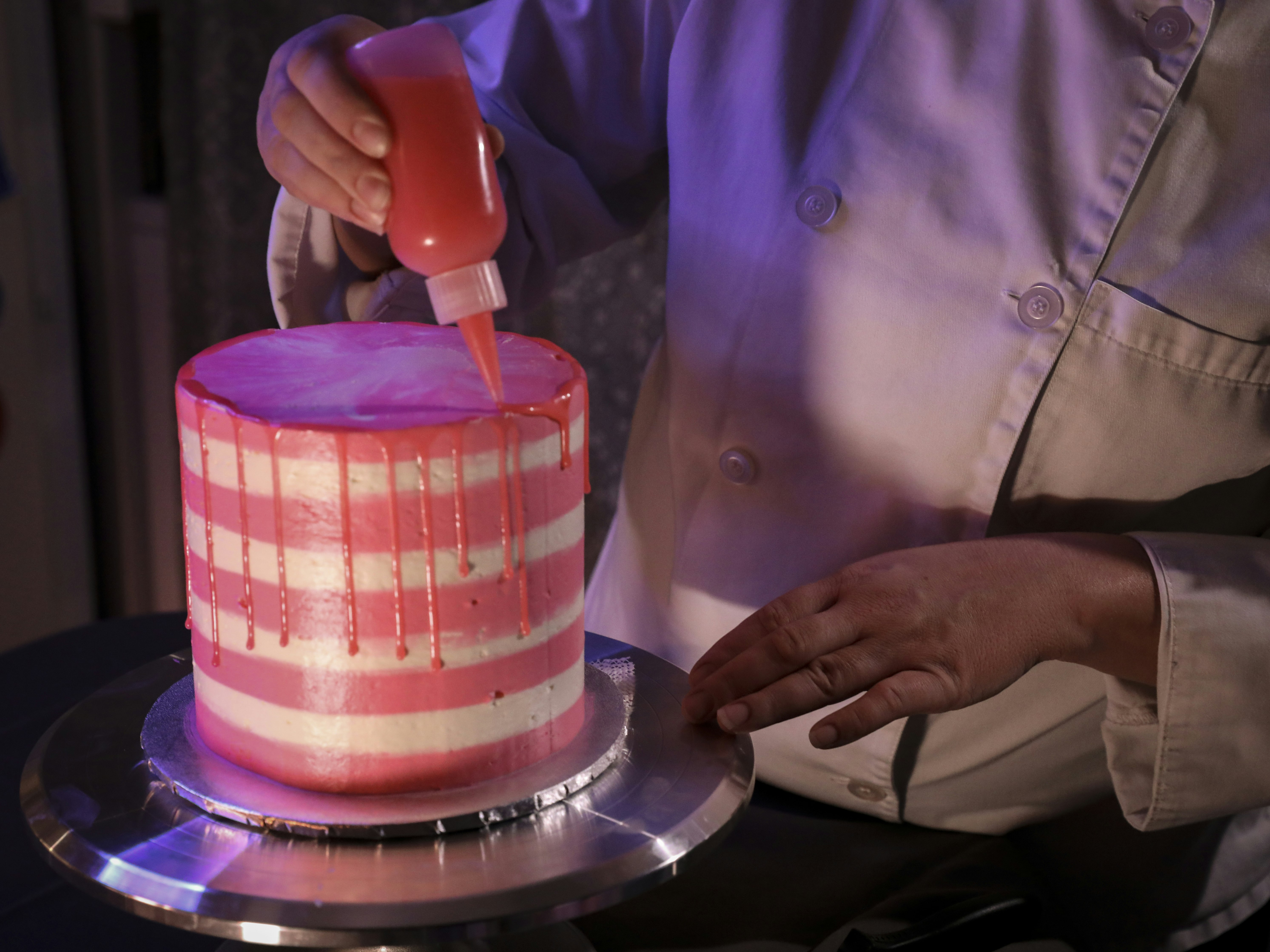 Piping pink buttercream onto a layer cake